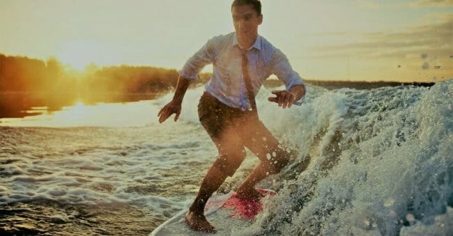 Young man in wet clothes surfboarding at summer resort