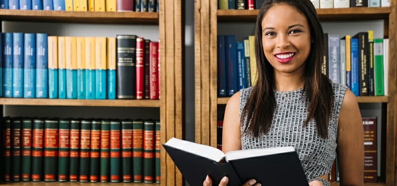 Young woman holding a book in front of bookshelf