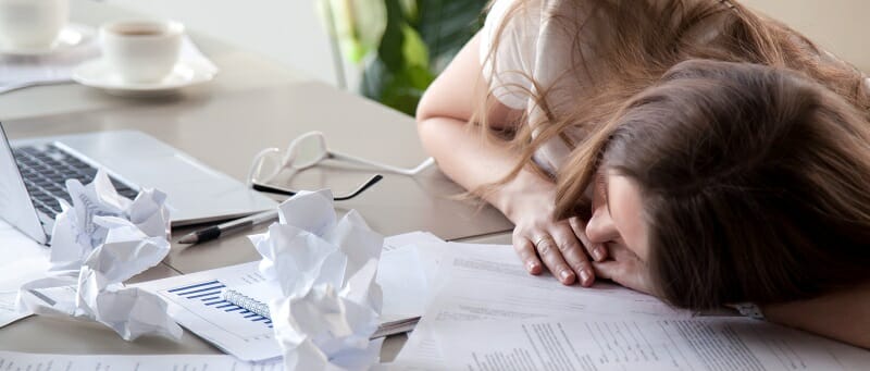 Woman sleeping on desk covered crumpled papers
