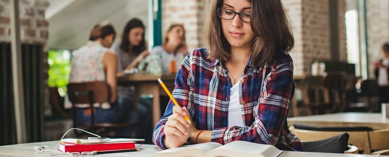 Young woman sitting alone studying with pencil in hand
