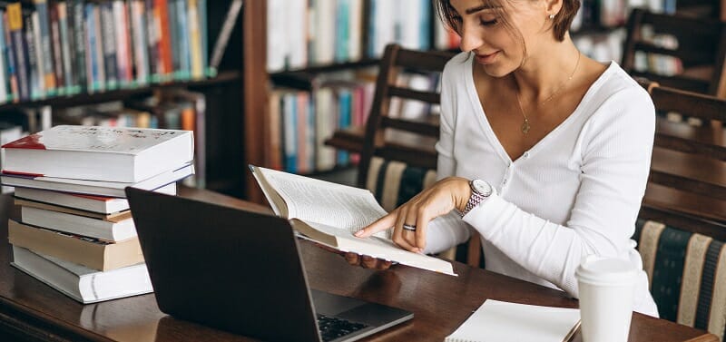 Young woman sitting at the library using books and computer