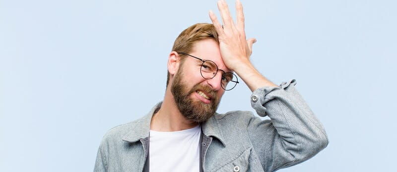 Young blonde man raising palm to forehead thinking oops, after making a stupid mistake or remembering, feeling dumb
