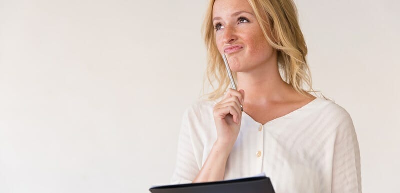 Pensive young woman holding pen and folder