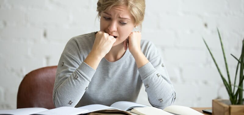 Portrait of a student girl sitting at the desk biting her fist