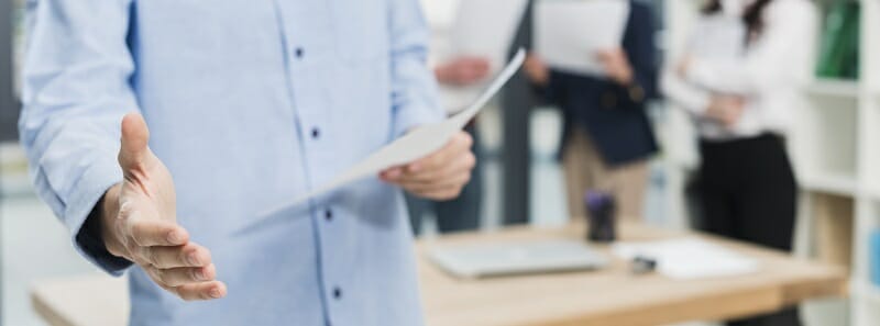 man holding paper in one hand, the other hand is extended for a handshake